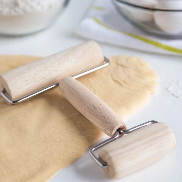 Two wooden rolling pins with metal handles, one larger and one smaller, placed on a dough surface with flour around.