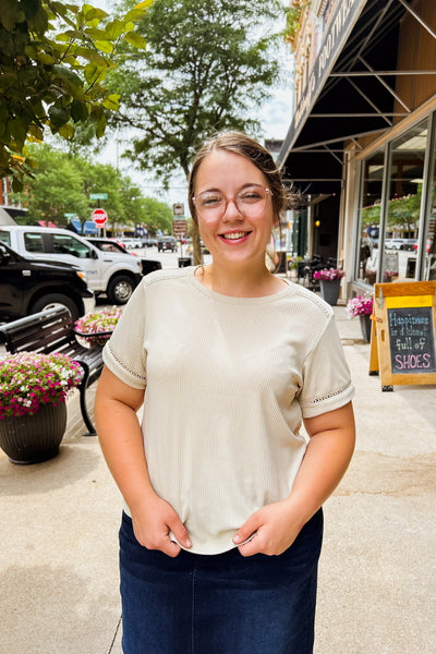 Woman wearing beige ribbed knit top with lace-trimmed shoulders and sleeves, styled with a denim skirt