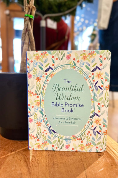 A book titled 'The Beautiful Wisdom Bible Promise Book' with a floral pattern on its cover, placed on a wooden surface.