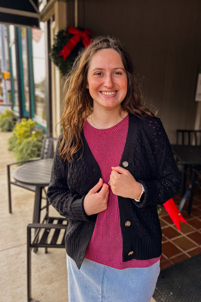 Woman wearing a black Pam Button Cardigan with pointelle knit, button up, relaxed fit, layered over a wine colored top
