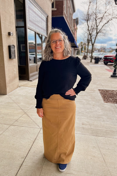 Woman wearing a khaki long denim skirt with comfort waistband, front and back pockets, paired with long sleeve black top.