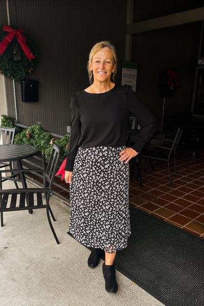 Woman wearing black floral A-line skirt with comfort waistband, sheer overlay, and full lining, styled with a long sleeve black top