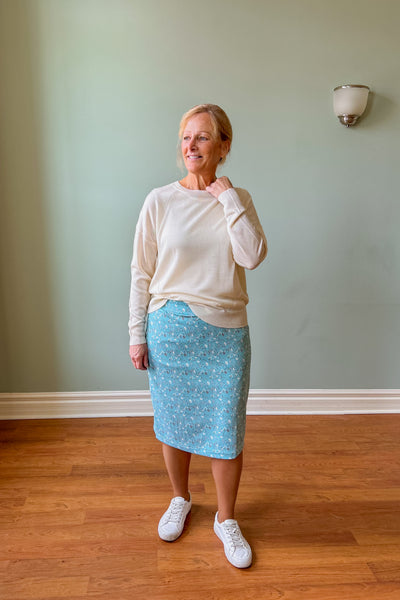 Woman wearing blue floral French Terry midi skirt with comfort waistband and modified pencil fit, styled with a cream sweater