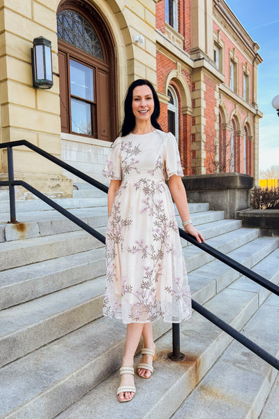 Woman wearing purple floral lace midi dress with embroidery, elastic back waist, and keyhole closure.