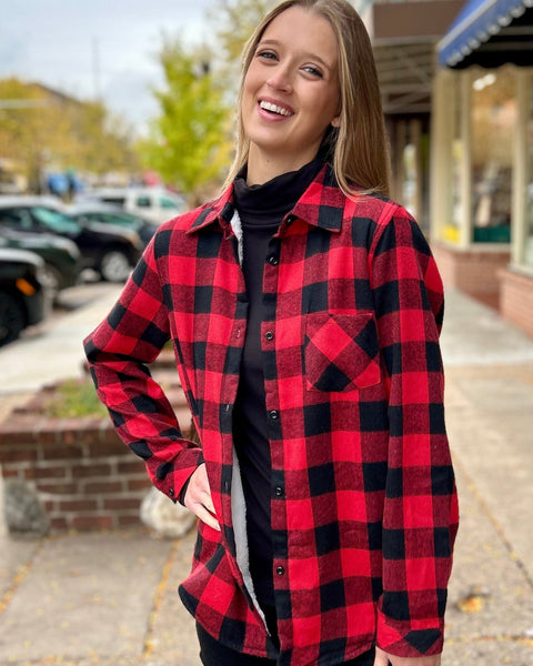 Young woman wearing a red and black sherpa-lined flannel over a black top, standing on a charming downtown sidewalk in fall.