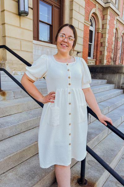 Woman wearing cream textured knit button-front dress with square neckline, patch pockets, and lined skirt.