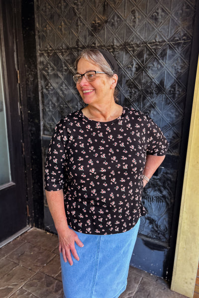 Woman wearing black floral ribbed knit top with elbow-length sleeves, modest neckline, and slightly fitted feminine shape.