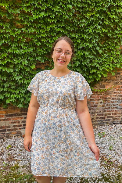 Woman wearing soft floral midi dress with flutter sleeves, modest neckline, elastic waist, and keyhole back closure.
