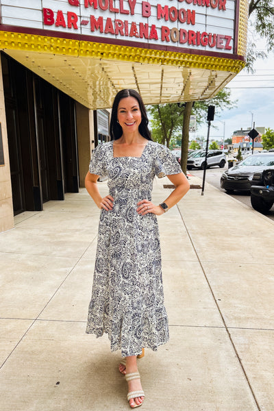 Woman wearing blue and white midi dress with square neckline, puff sleeves, elastic waist, and ruffled hem.