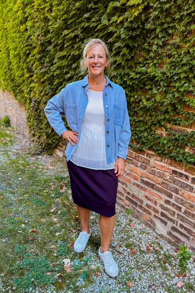 Woman wearing a plum knit midi skirt with comfort waistband and modified pencil fit, styled with a white top and denim jacket