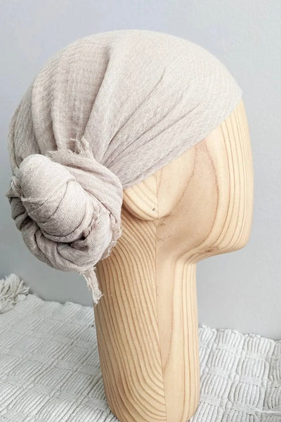 A beige gauze scarf displayed on a mannequin head, showing how it can be worn as a head covering.