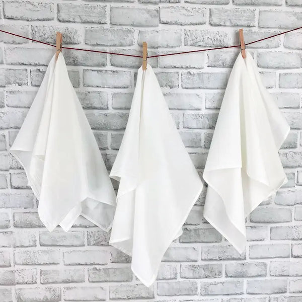 Three white cotton flour sack towels hanging on a clothesline against a brick wall backdrop.