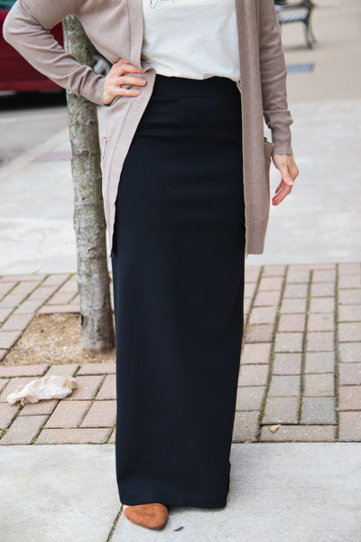 Woman wearing black ponte maxi skirt with comfort waistband, styled with a white top and cardigan.