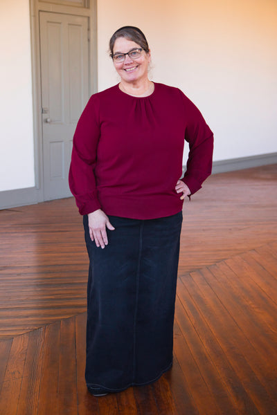 Woman wearing long black washed denim skirt with comfort waistband, front and back pockets, styled with red long sleeve top.