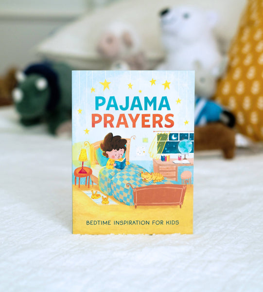 Children's book titled 'Pajama Prayers' on a bed with toys in the background