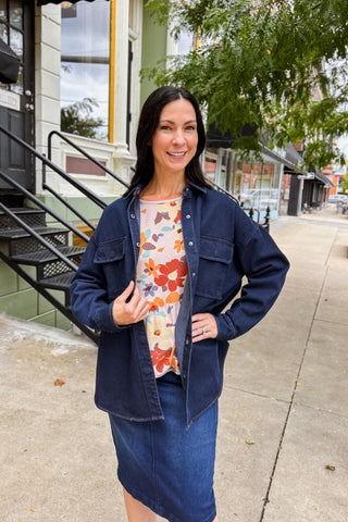 Woman wearing oversized dark indigo denim hacket with snap buttons and front pockets, styled with a floral blouse and denim skirt