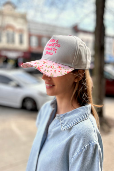 Woman wearing a cap with floral visor and text, standing outdoors.