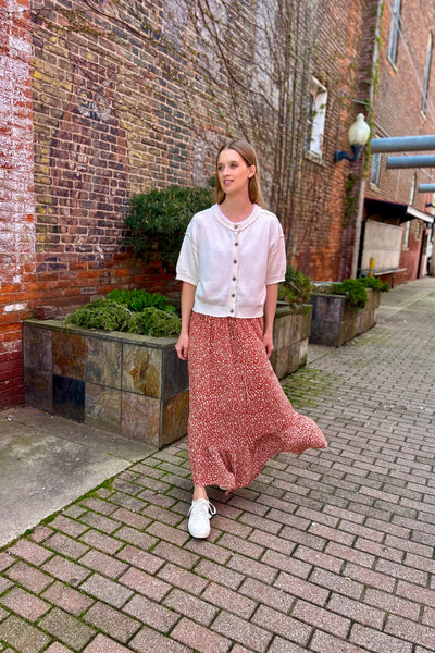 Woman walking on a brick sidewalk in an urban setting wearing flowy skirt.