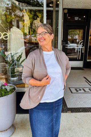 Woman wearing mocha ruffled cardigan in with curved front line and long sleeves, layered over a white tee with denim skirt