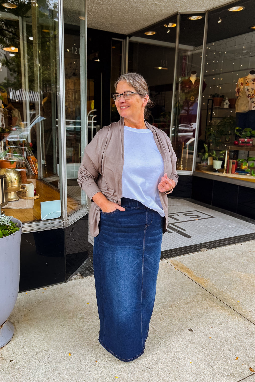 Woman wearing long dark wash denim skirt with elastic waist styled with a white tee and mocha cardigan