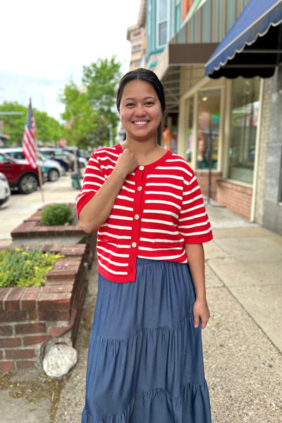 Woman wearing a red and white striped short sleeve sweater top with button-front detail and ribbed hem paired with a blue tiered maxi skirt for modest everyday style.