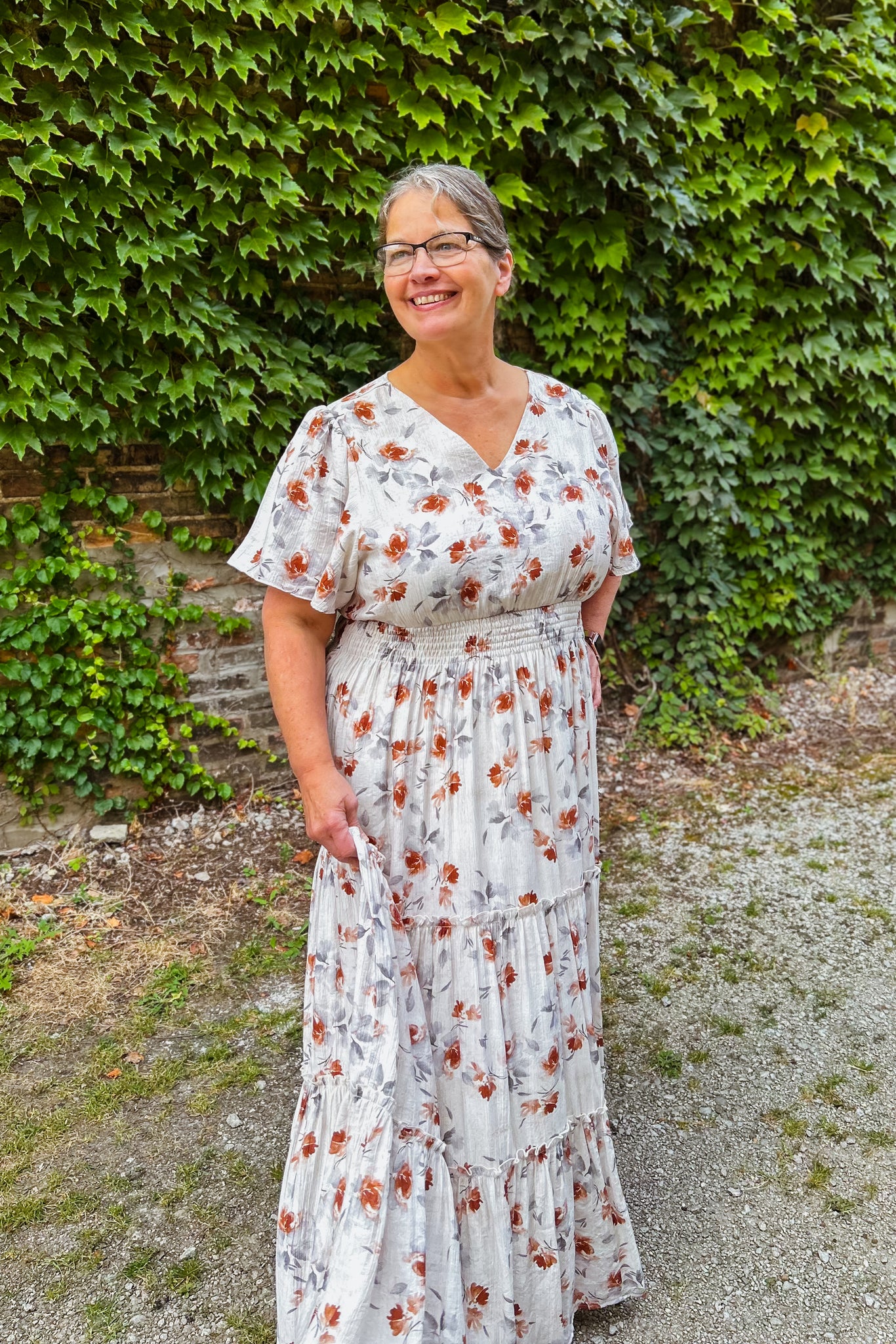 Woman wearing a floral dress standing in front of a green ivy-covered wall.