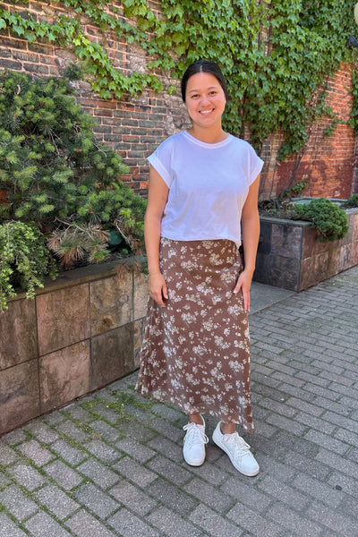 Woman wearing a brown floral chiffon maxi skirt with an elastic waist and flowing silhouette, styled with a white top for modern modest fashion.