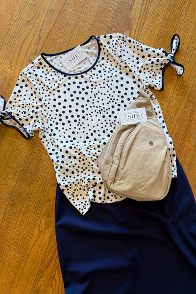Polka dot top, navy skirt, and beige bag on a wooden floor
