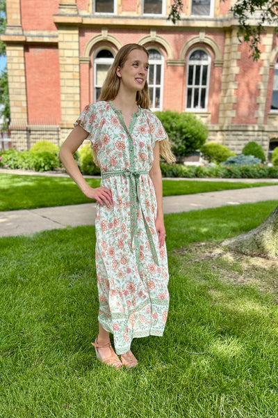 Lady wearing a modest flutter sleeve floral dress standing in front of an old courthouse. 