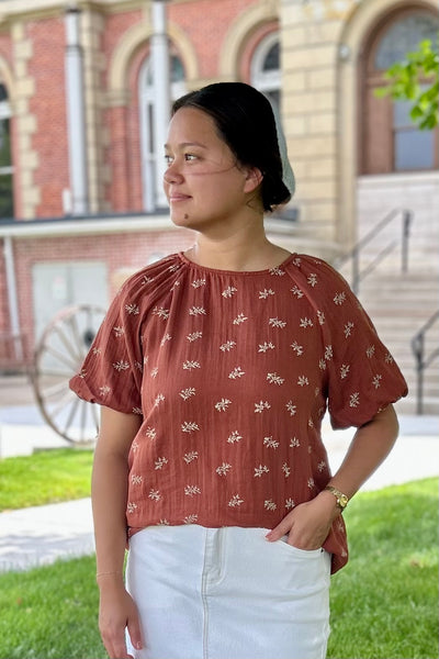 Woman wearing a terra cotta modest top standing outside of courthouse.