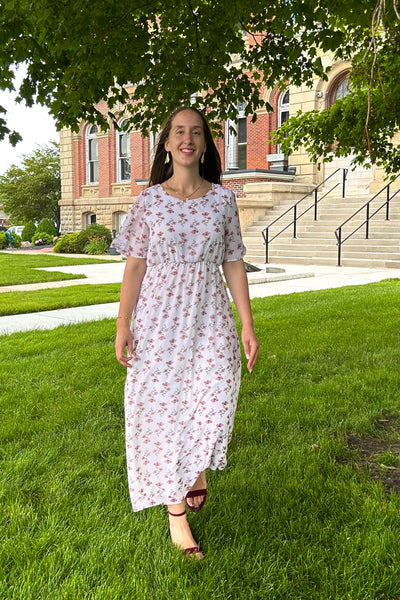 Woman wearing a modest floral maxi dress walking on the courthouse lawn.
