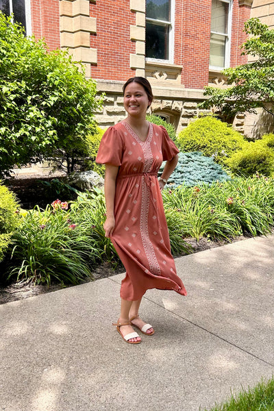 Ladies wearing an embroidered terra cotta dress standing a sidewalk in front of a brick building. 