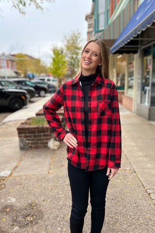 Young woman wearing a red and black sherpa-lined flannel over a black top, standing on a charming downtown sidewalk in fall.