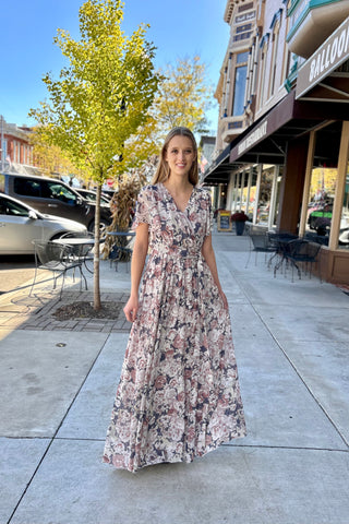 Woman in a floral dress V-neck dress  standing on a sidewalk with shops in the background.