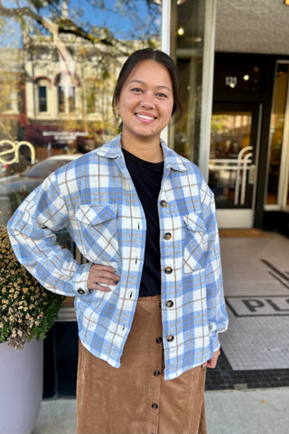 Light blue plaid flannel shacket with button-front closure and chest pockets, styled as a cozy layering piece for cool-weather days.