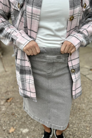 Person wearing a plaid shirt over a white top and gray skirt on a sidewalk.
