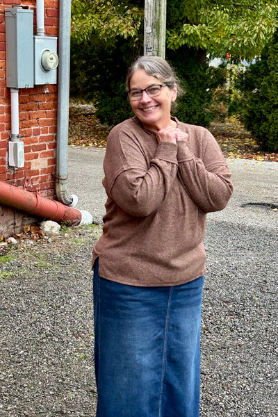 Woman wearing a cozy brown top standing outside near an alley 