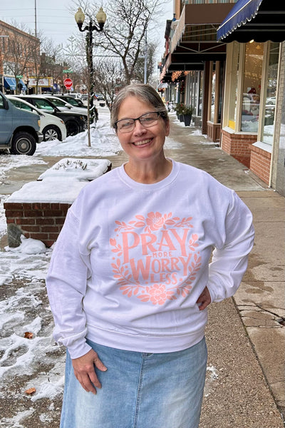 Woman wearing a white sweatshirt with a pink design and text, standing on a snowy sidewalk.