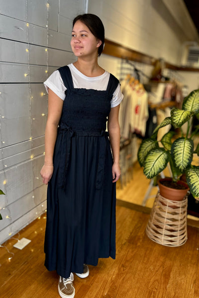 Woman wearing a navy blue dress over a white shirt in a store setting.