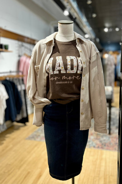 Mannequin wearing a beige shirt over a brown graphic t-shirt with text in a store setting.