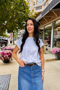 Woman wearing white soft cotton rolled sleeve top with round neckline and relaxed fit, styled tucked into denim skirt with a belt. 