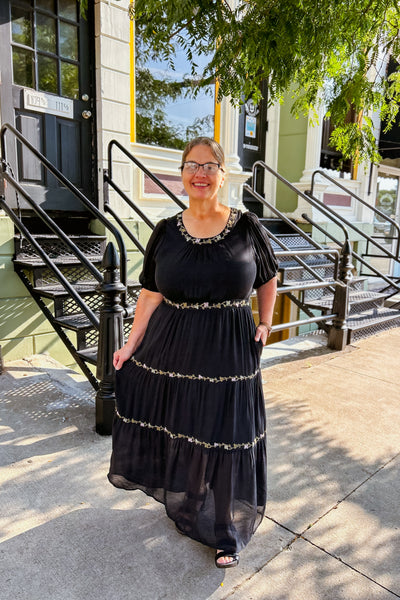 Woman wearing black tiered maxi dress with delicate embroidery and flowing silhouette, styled for a special occasion.