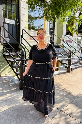 Woman wearing black tiered maxi dress with delicate embroidery and flowing silhouette, styled for a special occasion.